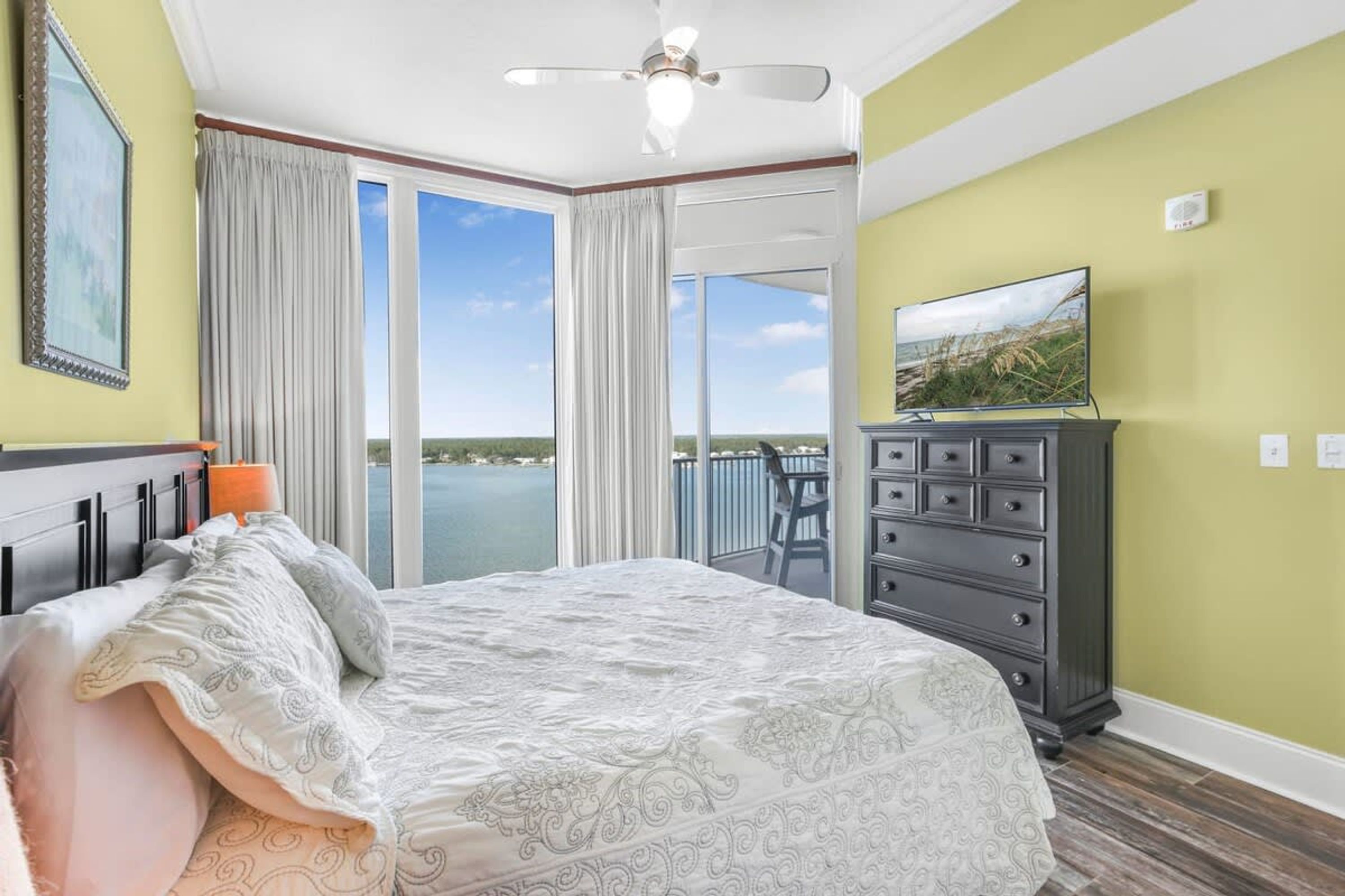 A bedroom with a bed, a dresser, a television, and a view of the outdoors.
