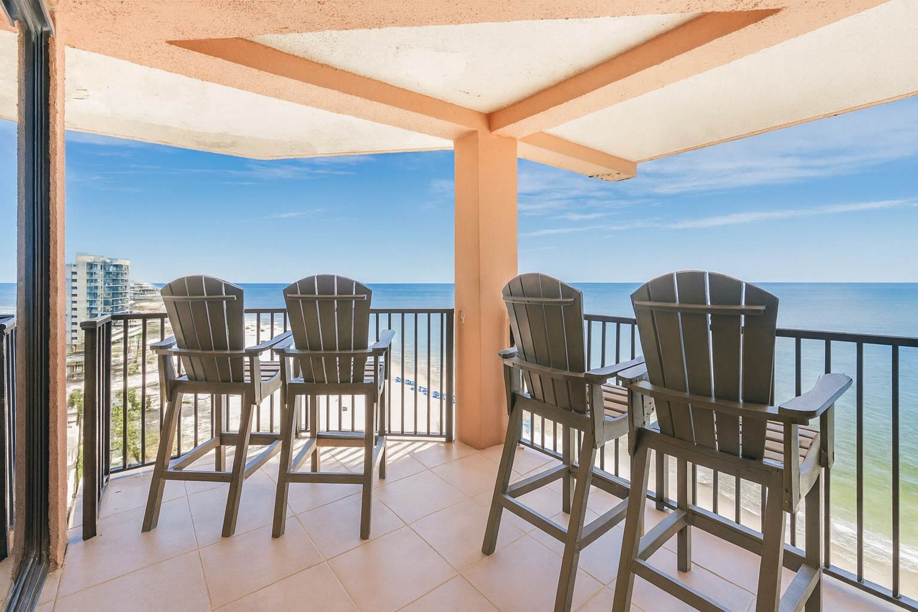 A balcony with three Adirondack chairs facing a beach.