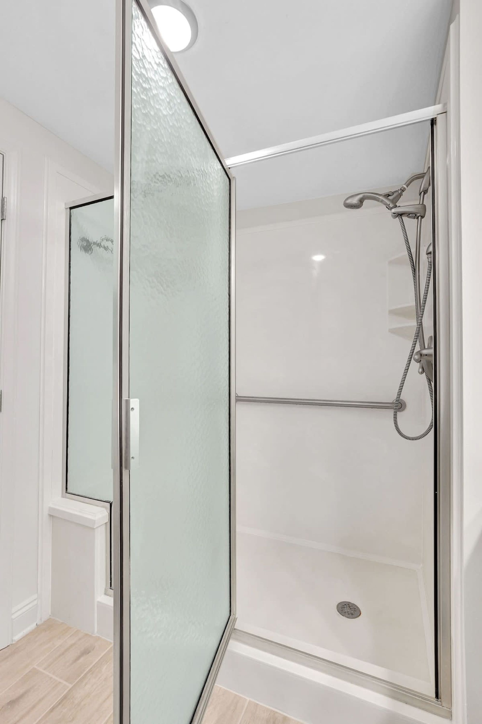 A modern bathroom with a glass shower enclosure, a visible drain, and a white tiled floor.
