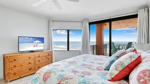Une chambre à coucher avec un lit, une télévision, une commode en bois et un balcon offrant une vue sur l’océan.