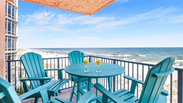 Un balcon offrant une vue sur l’océan, avec une table sur laquelle sont posés deux verres de jus d’orange et quatre chaises Adirondack vertes.