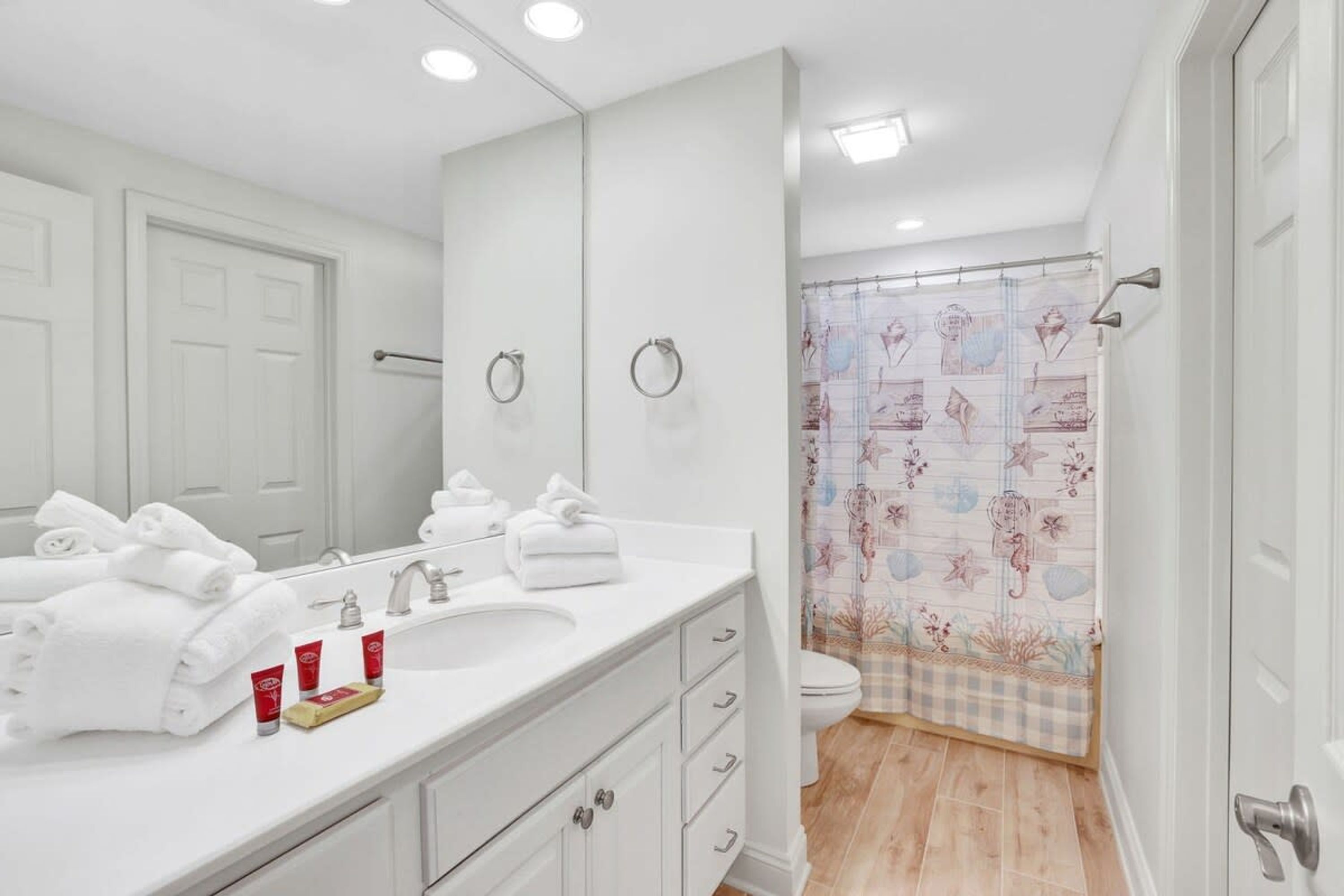 A bathroom with a white vanity, a large mirror, a toilet, and a shower curtain with a floral pattern.
