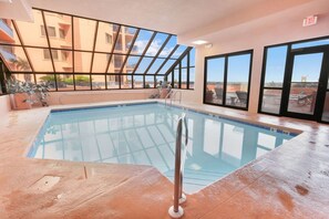 An indoor swimming pool with clear glass walls, a metal ladder, and a view of a building with balconies. - Four Seasons 402-e Private Fishing Pier (Orange Beach)