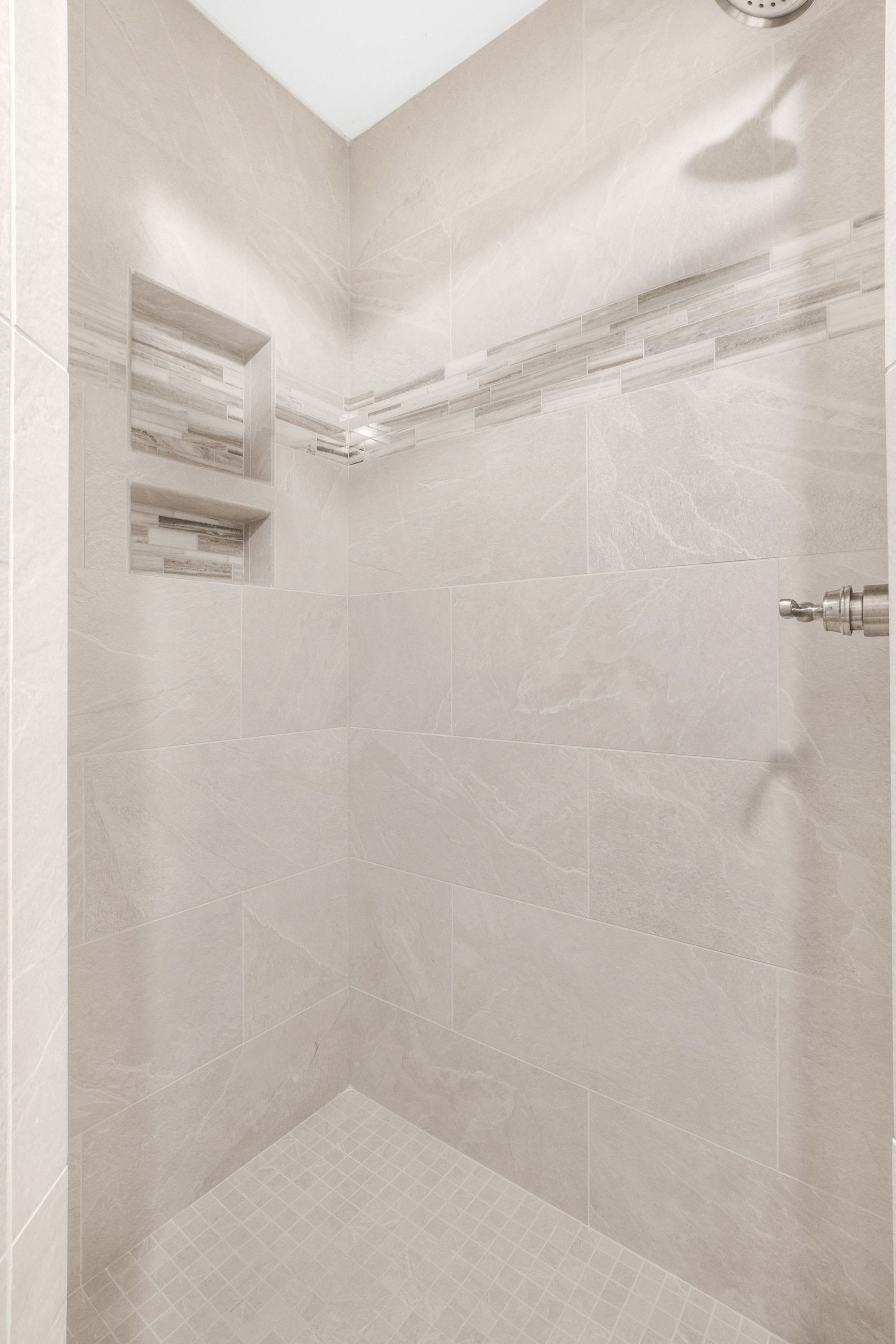 Een moderne douche met een betegelde wand en een ingebouwd schap.