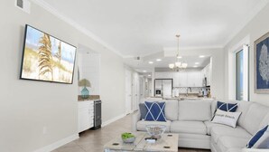 A modern living room with a white sofa, a coffee table, and a TV mounted on the wall. - Enclave 401 Beachfront Tennis Stunning Views (Orange Beach)