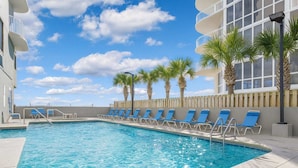 A swimming pool with blue chairs and palm trees, surrounded by a building with balconies. - Island Royale- Beachfront Penthouse (Gulf Shores)