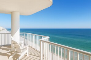 Un balcon avec des balustrades blanches, un parasol blanc et une rangée de chaises longues blanches donnant sur un océan bleu et limpide.