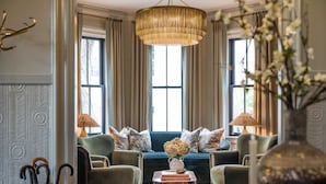 A room with a large window, a sofa, two armchairs, a coffee table, and a chandelier. - The Royce - Two Luxury Family Homes in Downtown Newport (Newport)