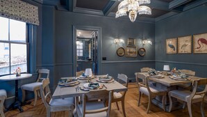 A dining area with wooden tables and chairs, a chandelier, and wall-mounted artwork. - The Royce - Two Luxury Family Homes in Downtown Newport (Newport)