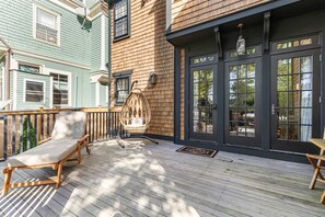 A wooden deck with a lounge chair and a wicker chair, a black door with glass panels, and a wooden fence. - The Royce on Spring - High-end Family Getaway in Newport (Newport)