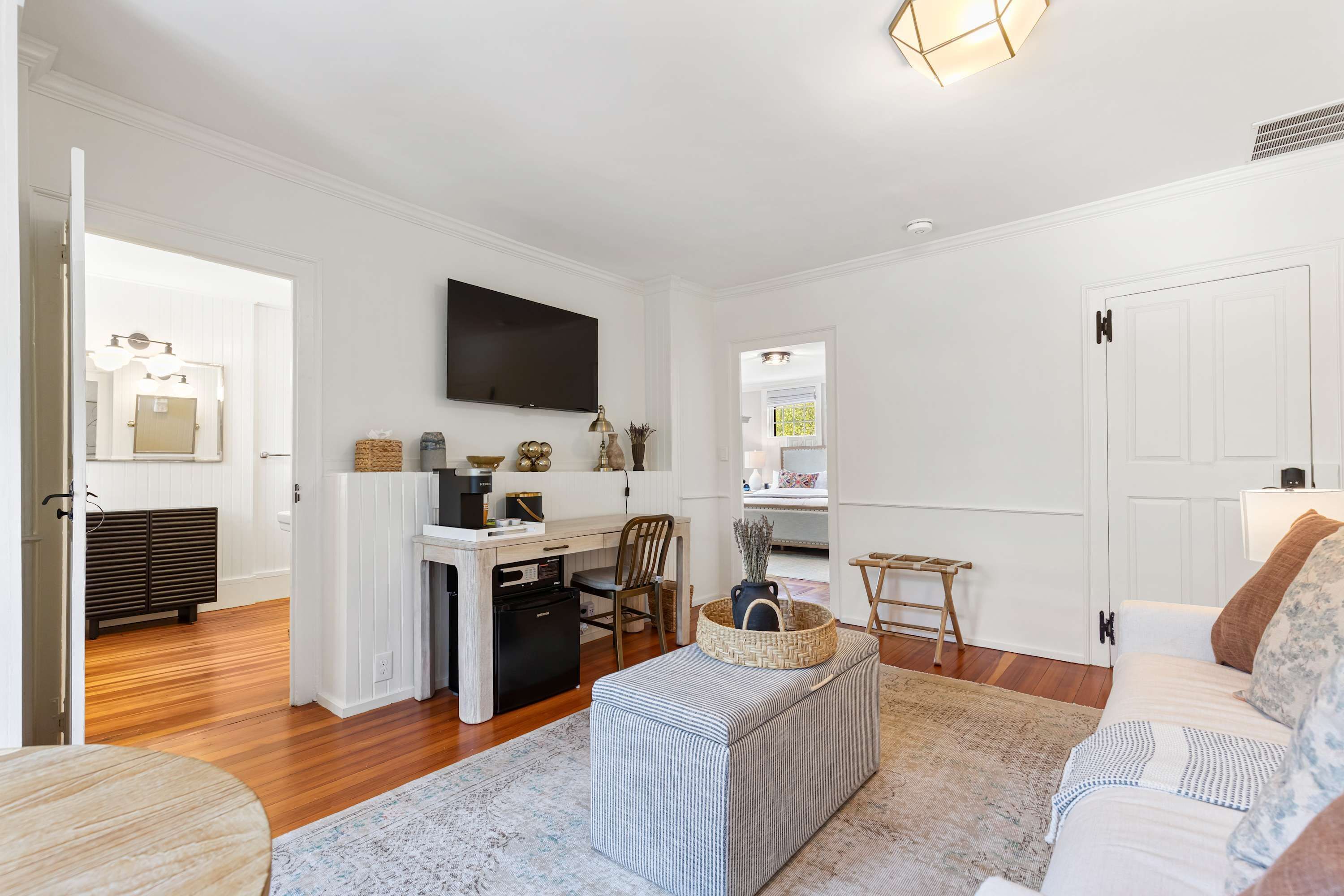 A modern living room with a flat-screen TV, a dining area with a table and chairs, a kitchen with a refrigerator, and a cozy seating area with a sofa and ottoman.