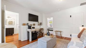 A modern living room with a flat-screen TV, a dining area with a table and chairs, a kitchen with a refrigerator, and a cozy seating area with a sofa and ottoman.