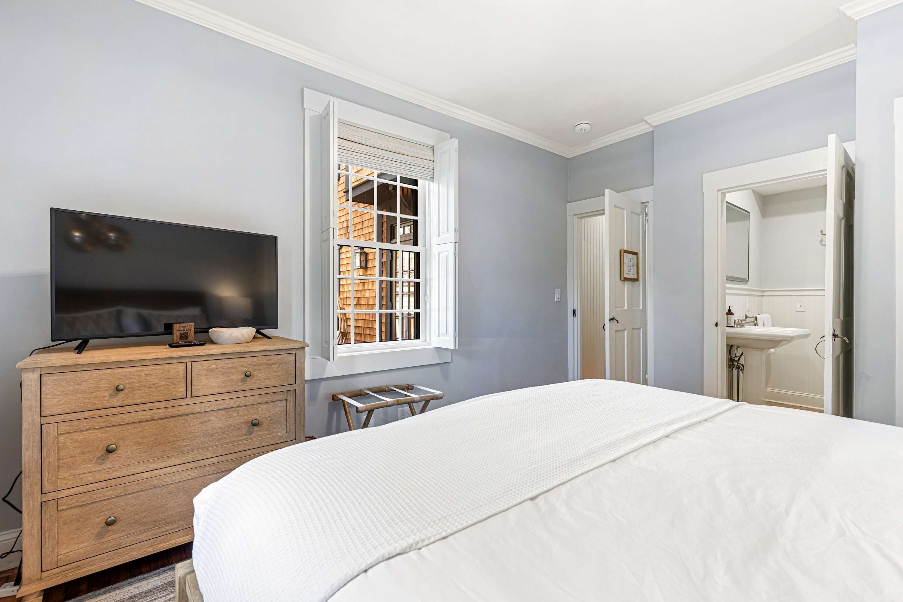A bedroom with a bed, dresser, TV, window, and bathroom.