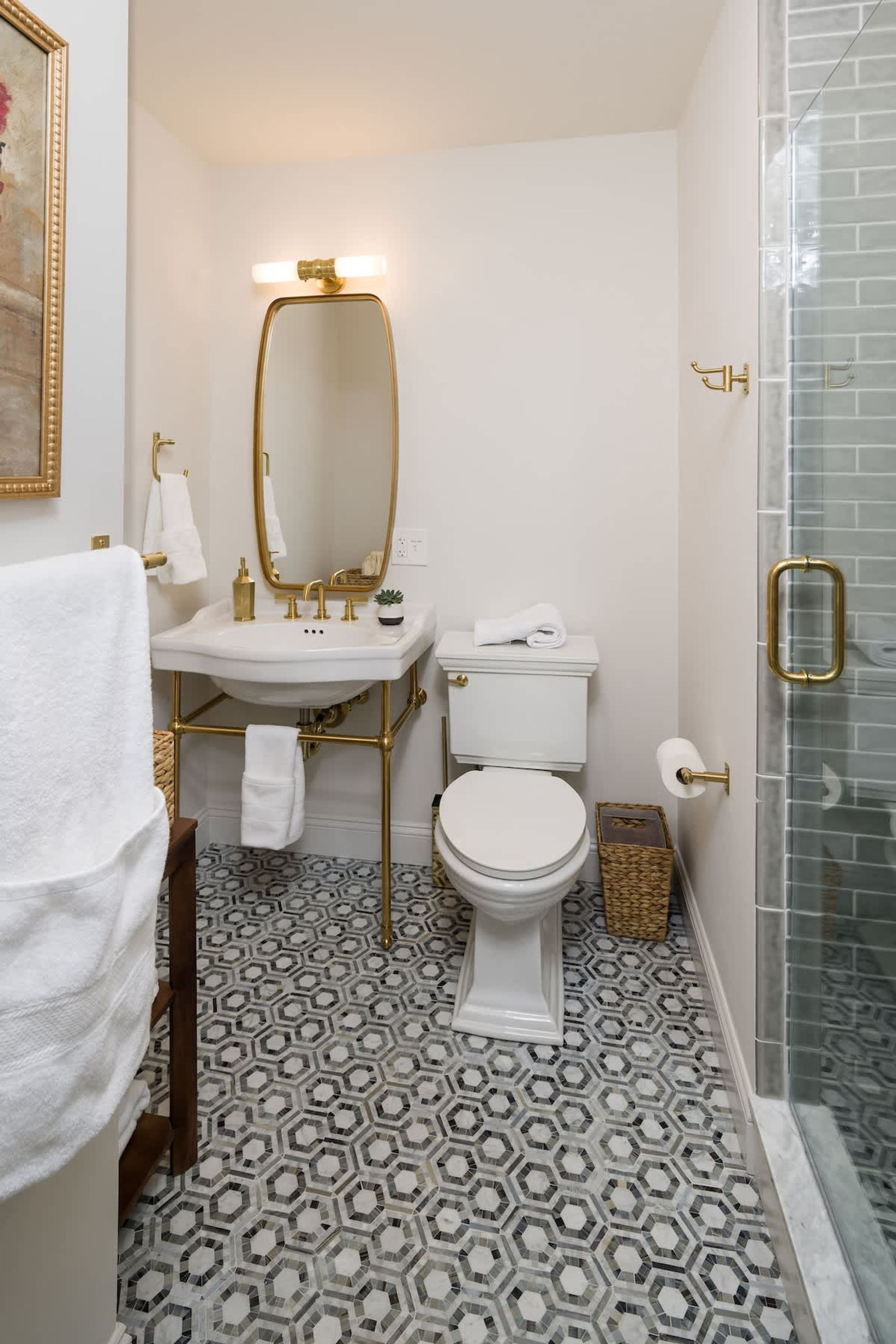 A bathroom with a white sink, gold fixtures, a white toilet, and a patterned floor.