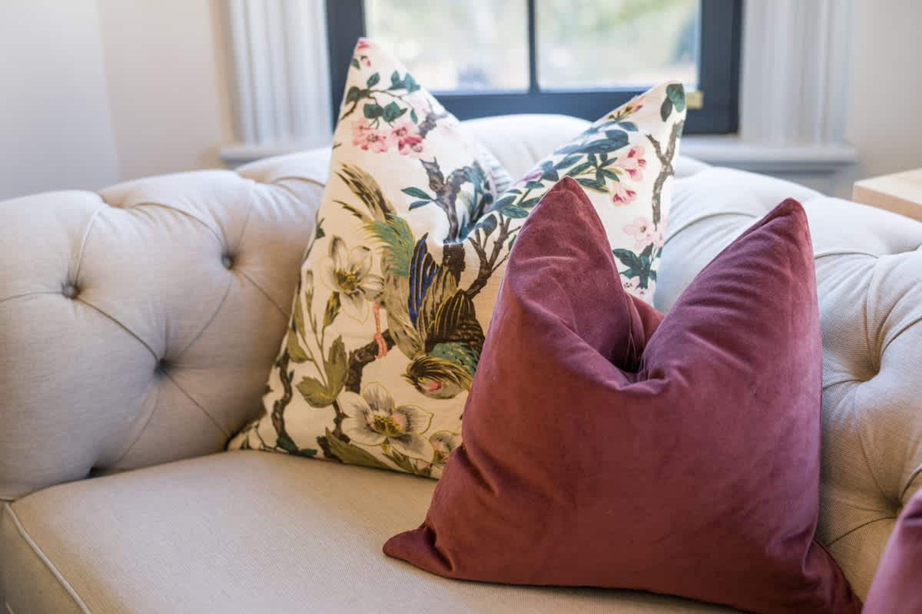 Un canapé à capitons, agrémenté de coussins à motifs floraux et unis.