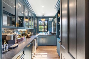 Une cuisine moderne avec des meubles de couleur bleu foncé, une hotte de cuisine en acier inoxydable et une grande fenêtre qui laisse entrer la lumière naturelle.