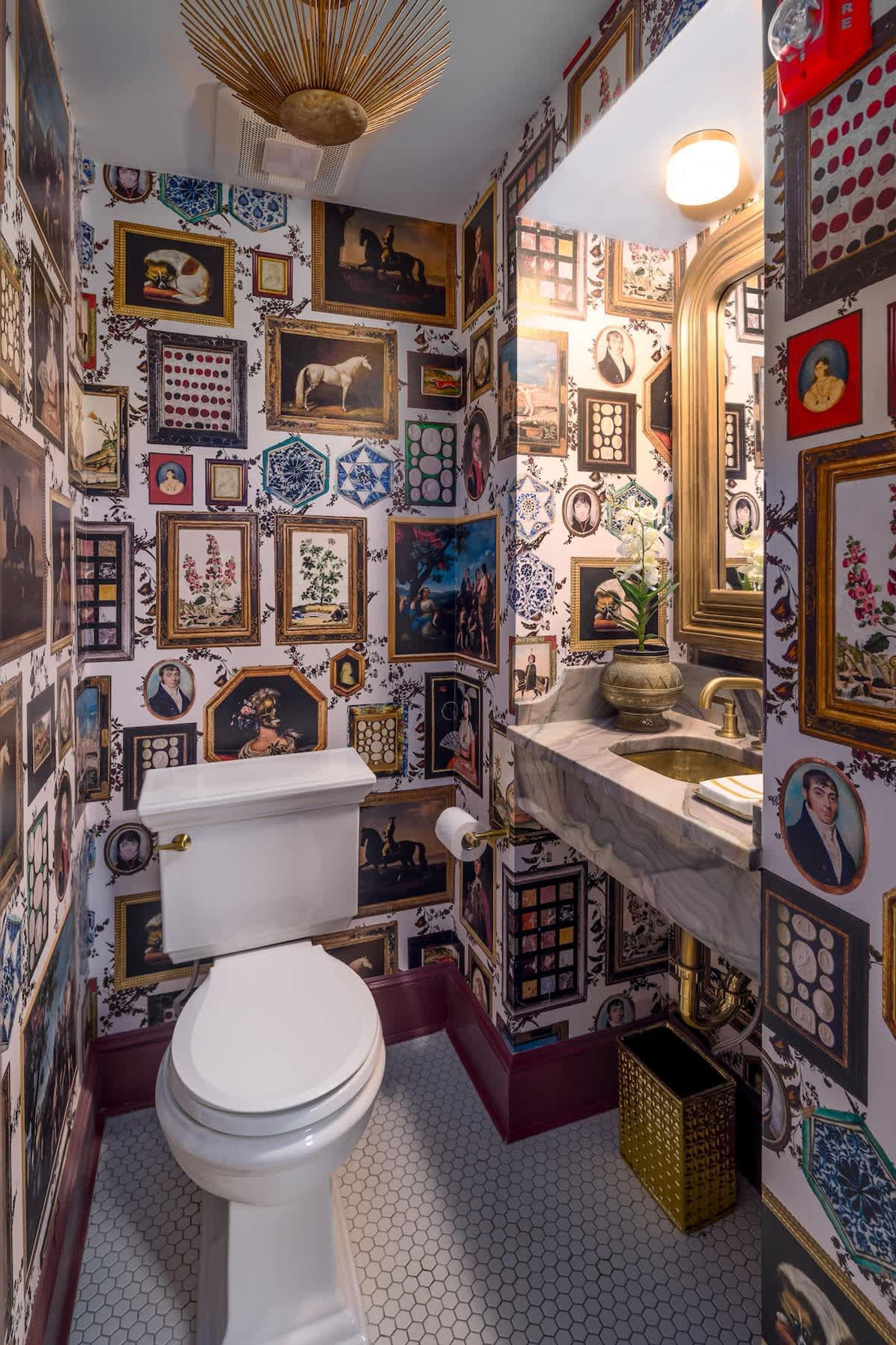 A bathroom with a toilet, sink, and mirror, decorated with numerous framed pictures and tiles.
