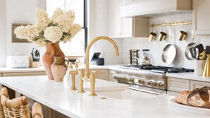 A modern kitchen with white cabinetry, a gold faucet, and a vase of flowers on the counter. - The Queen Anne Suite A Newport Seaside Retreat (Newport)