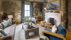 A living room with a fireplace, a sofa, a coffee table, and a blue armchair. - The Queen Anne Suite A Newport Seaside Retreat (Newport)