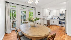 A modern kitchen with white cabinets, a central island, and a dining area with a wooden table and chairs. - Regatta Suite at The Royce Refined Newport Charm (Newport)