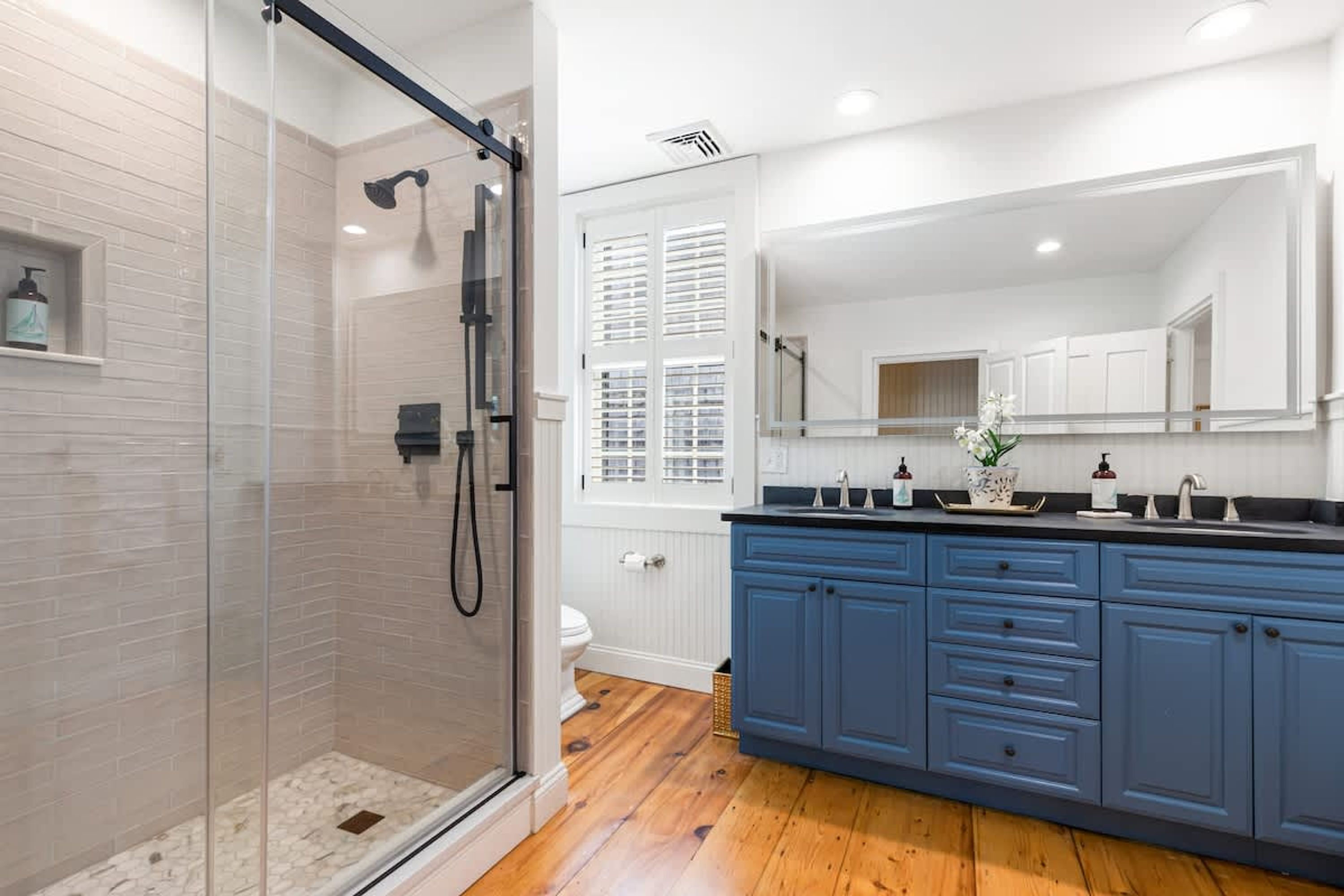 A modern bathroom with a glass shower enclosure, white tiled walls, and a wooden floor.