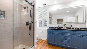 A modern bathroom with a glass shower enclosure, white tiled walls, and a wooden floor.