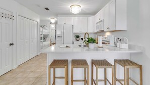 A modern kitchen with white cabinetry, a central island with stools, and a chandelier. - Grand Caribbean 201- Beach bay View 1 BR w Bunk (Orange Beach)