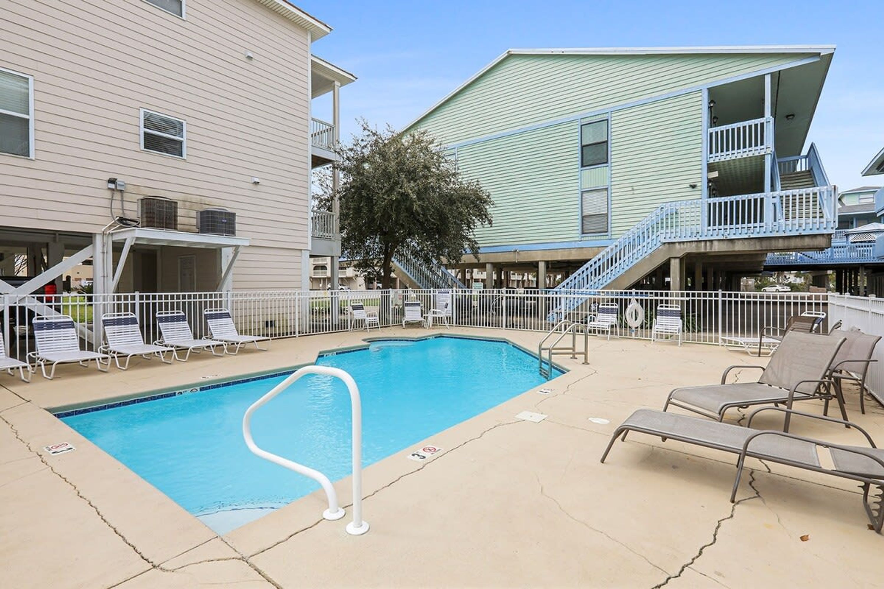 A swimming pool with lounge chairs and a staircase leading to a balcony.