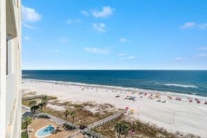 A beach view from a balcony with a pool, beach umbrellas, and a clear blue sky. - Windward Pointe 903- Beachfront Indoor Outdoor Pool (Orange Beach)