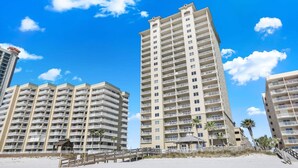 Un hotel frente a la playa con varios edificios altos, un paseo marítimo de madera y palmeras.