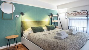 A neatly made bed with a quilted cover, a bedside table, a wall-mounted lamp, and a mirror. - Milan Central Station - Green Loft (Milano)