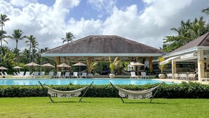 A pool area with lounge chairs and umbrellas, surrounded by palm trees and a covered pavilion. - The Beach View Playabonita Beachfront Pool (Las Terrenas)