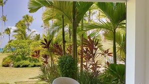A modern outdoor seating area with a white table, a wicker basket of towels, and a chair with a decorative pillow. - The Beach View Playabonita Beachfront Pool (Las Terrenas)
