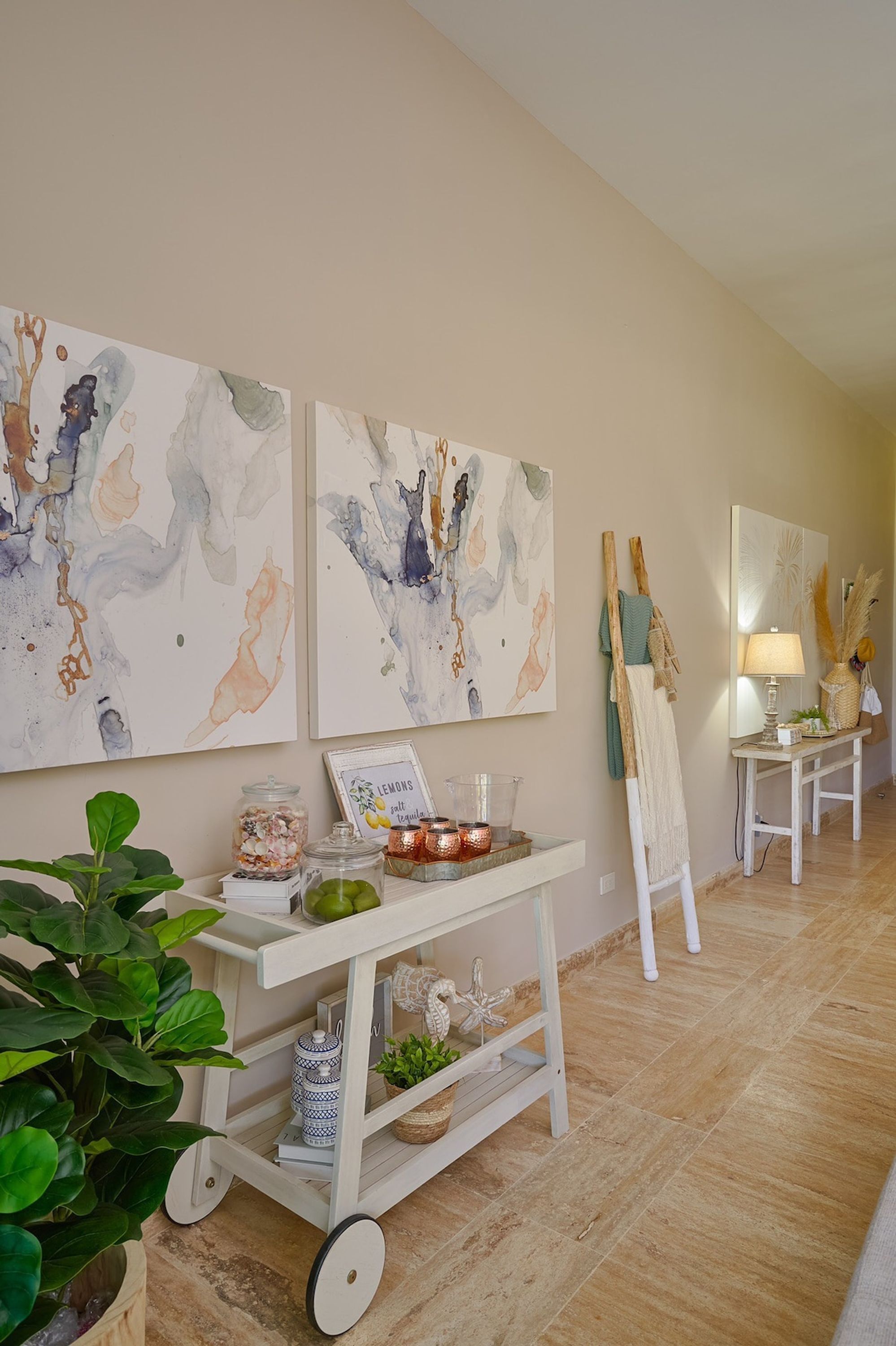 A hallway with abstract wall art, a white cart with decorative items, and a potted plant.