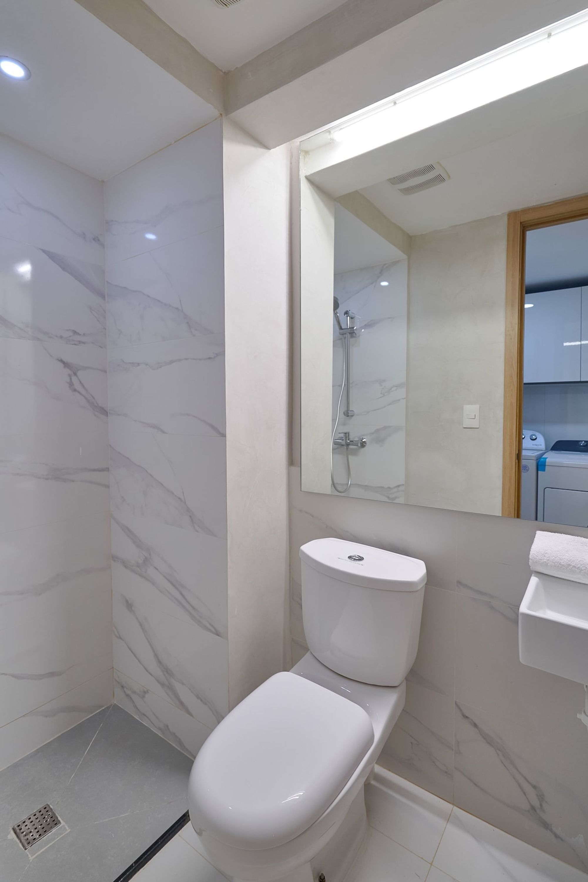 Un baño moderno con inodoro blanco, ducha y pared de mármol.