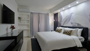 A modern bedroom with a large bed, a flat-screen TV, a desk, and a wall-mounted air conditioner. - 2BR The City Center Dtown Pool Gym Nearcecilip (Santo Domingo)