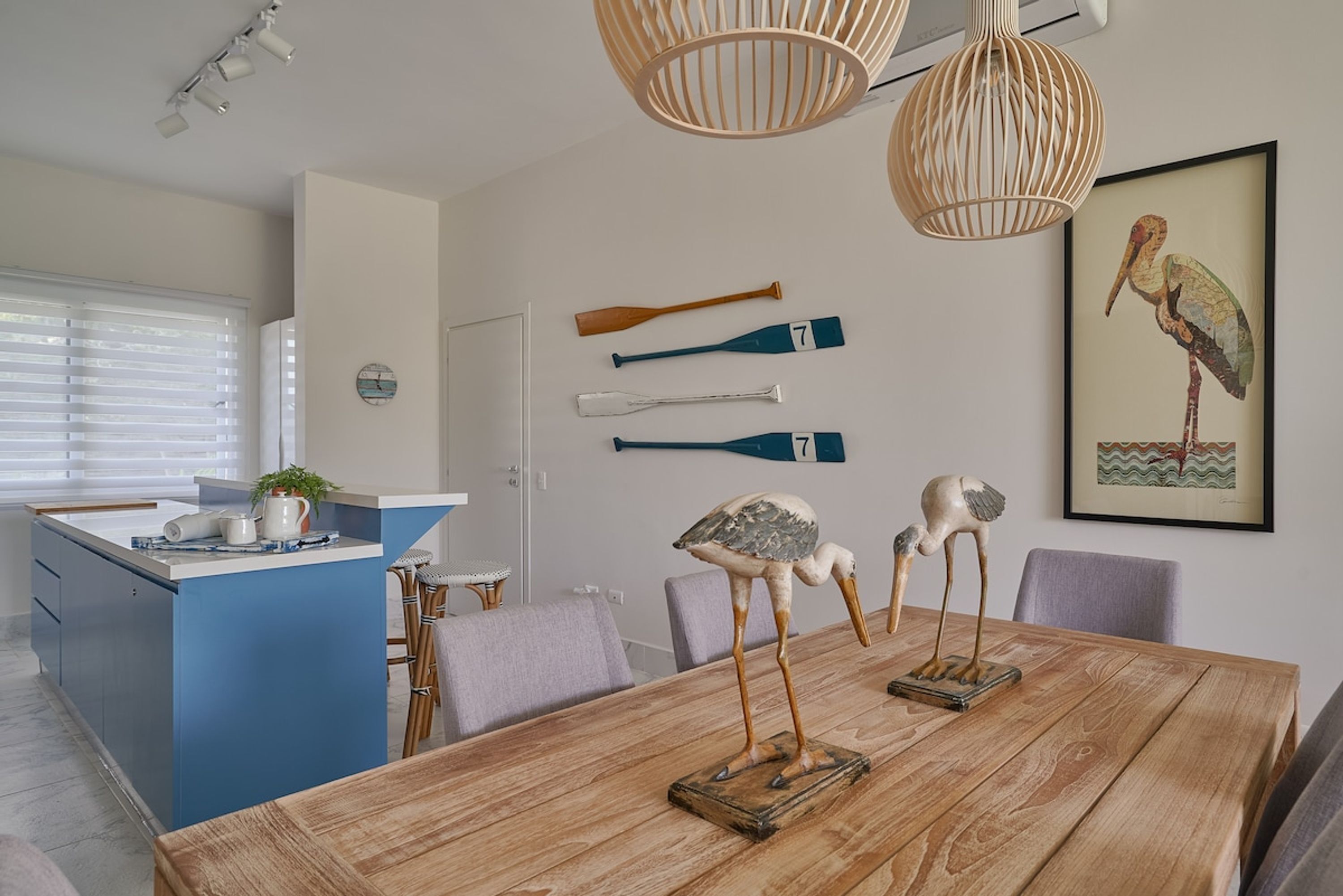 A modern kitchen with a blue island, wooden dining table, and decorative bird sculptures.