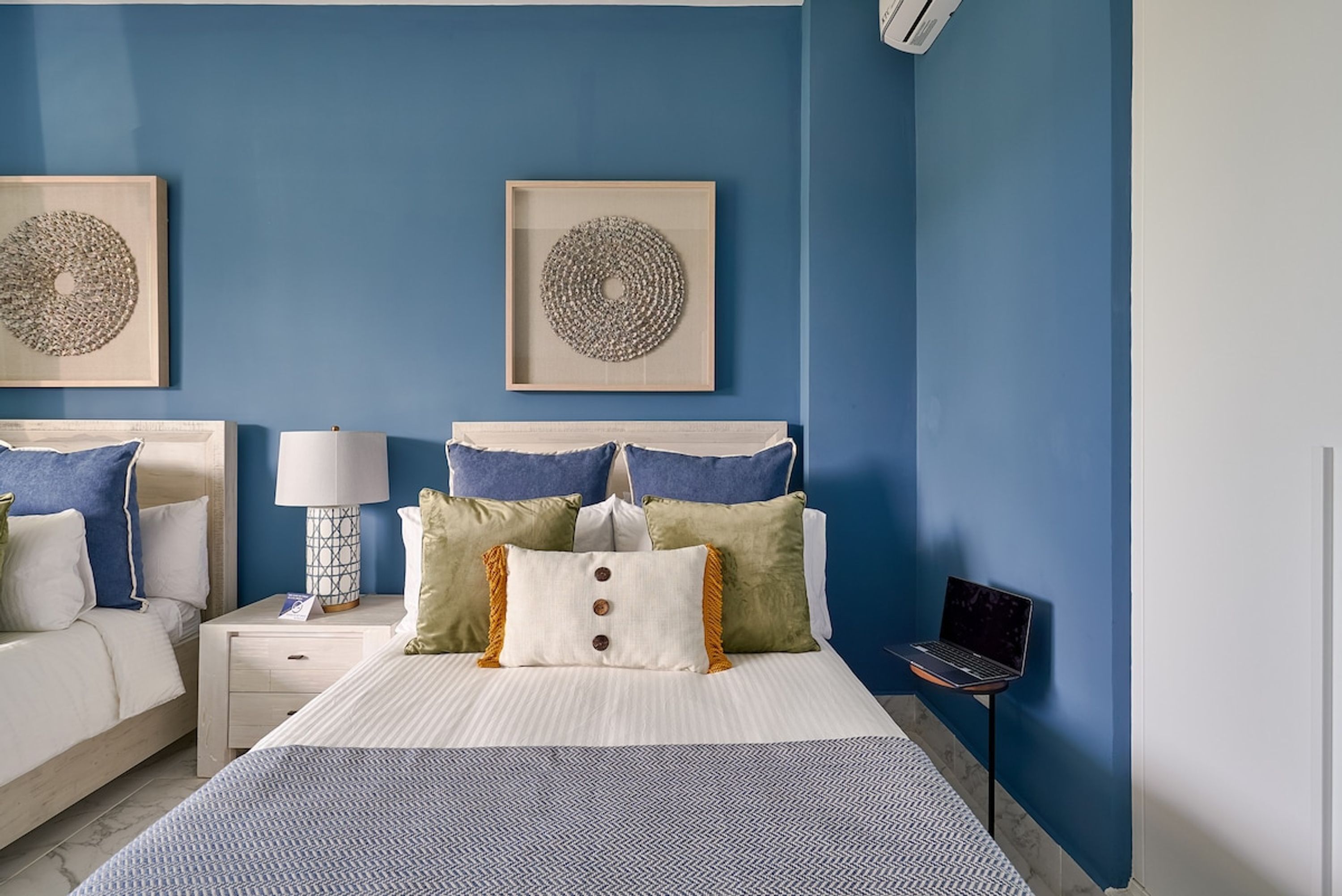 A bedroom with a bed, two bedside tables, a lamp, and a laptop on a stand.