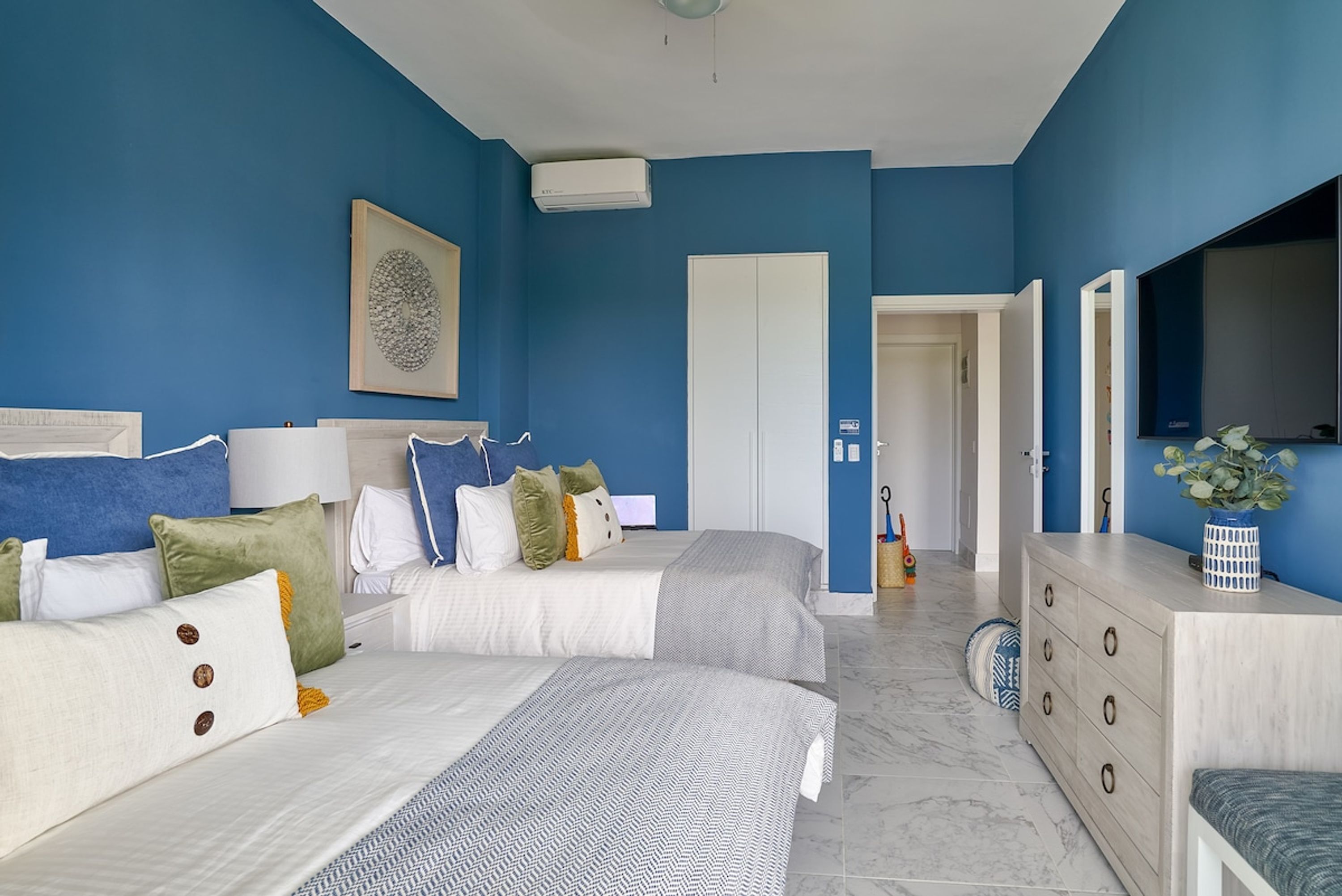 A bedroom with two beds, a dresser, a mirror, and a door leading to another room.