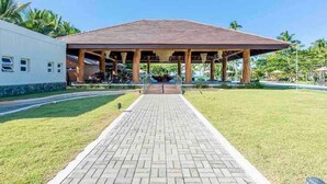 Un pavillon abrité, auquel on accède par une allée dallée, est entouré d’une pelouse bien entretenue et de palmiers.