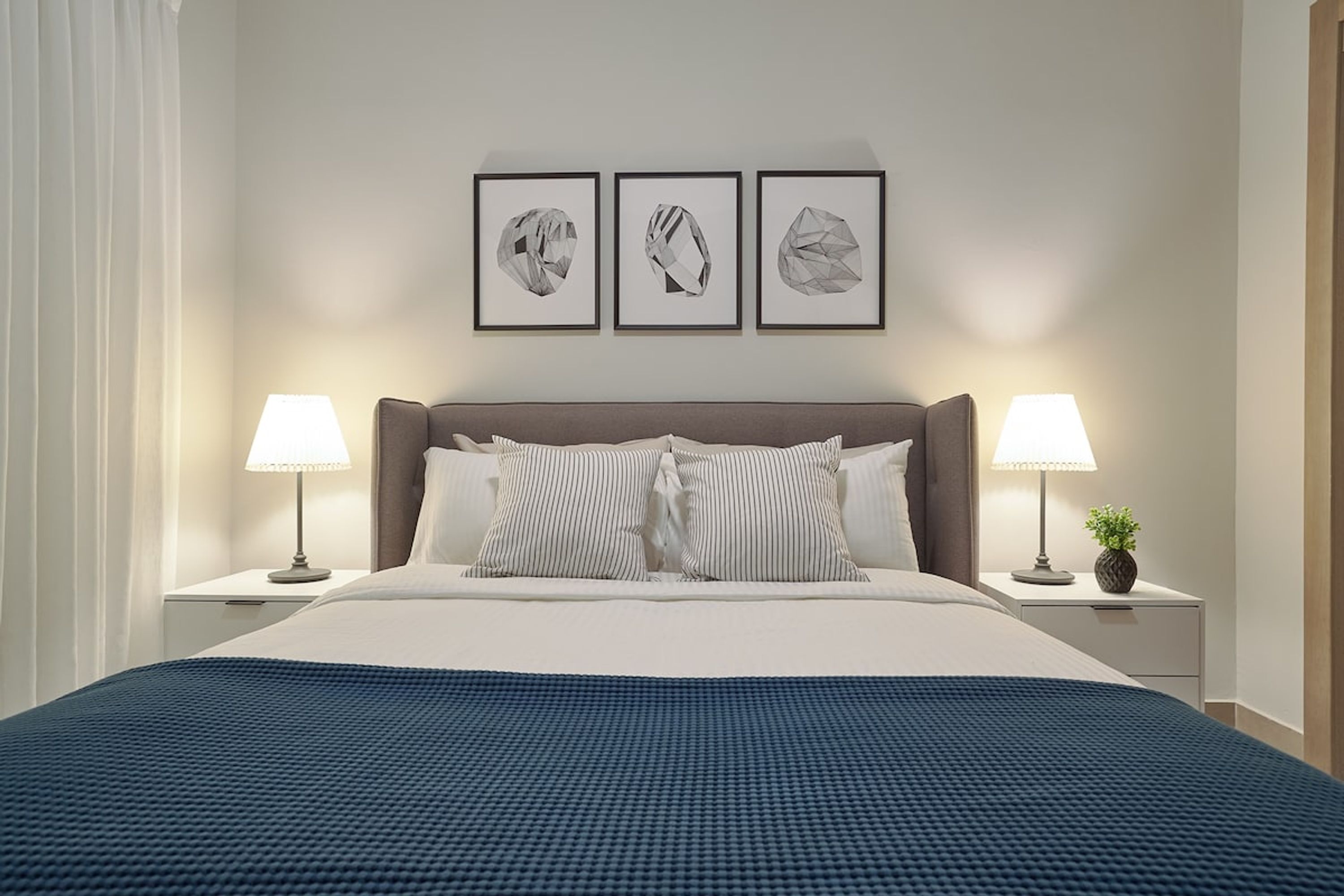 A neatly made bed with a blue blanket, two bedside lamps, and three framed pictures on the wall.