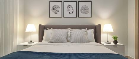 A neatly made bed with a blue blanket, two bedside lamps, and three framed pictures on the wall.