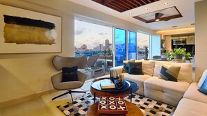 A modern living room with a city view, a large painting, and a cozy seating area. - Acqualina s View Santo Domingo (Santo Domingo)