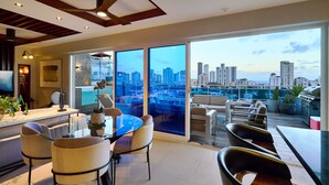 A modern living room with a glass dining table, comfortable seating, a city view, and a ceiling fan. - Acqualina s View Santo Domingo (Santo Domingo)