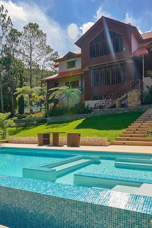 A modern house with a swimming pool, surrounded by a well-maintained lawn and trees. - 4BR Wood Mountain Villa Jarabacoa Heated Pool (Jarabacoa)