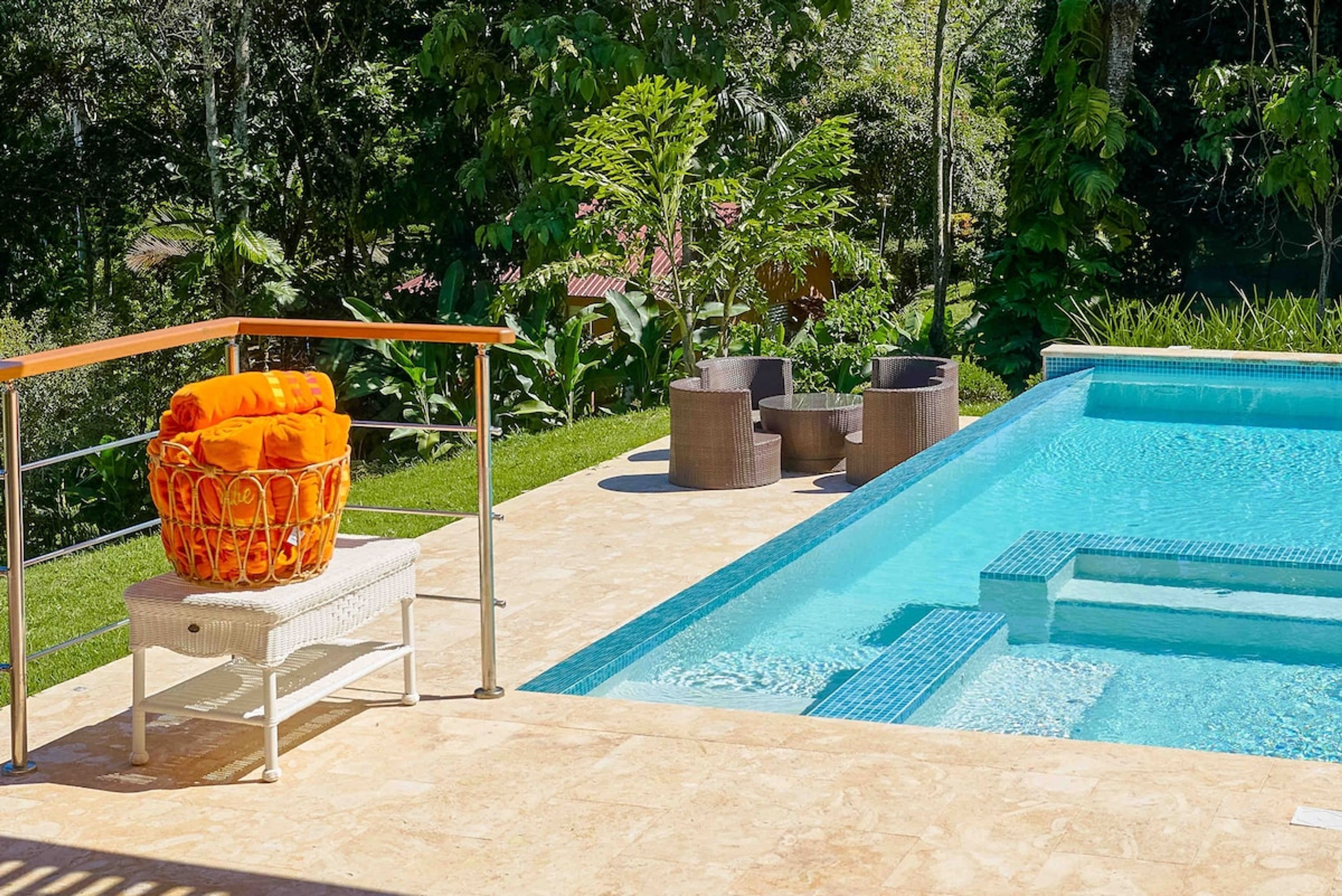 Uma piscina com borda azulejada, rodeada por móveis de exterior e um banco de vime.