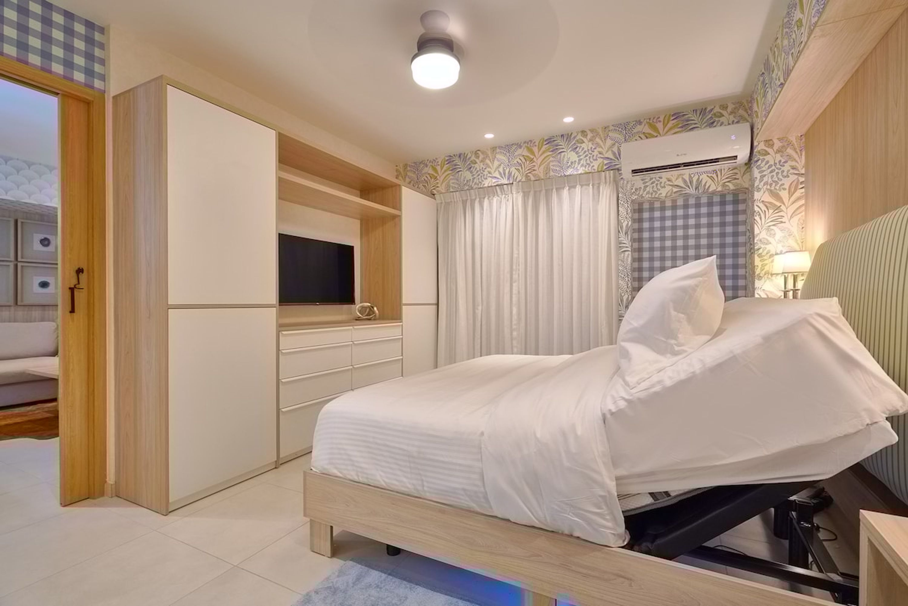 A bedroom with a bed, a wardrobe, a television, and an air conditioning unit.