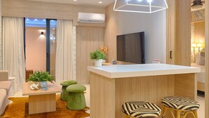A modern living room with a wooden floor, a sofa, a coffee table, and a TV. There is a kitchen area with a bar and stools. - Peaceful Retreat Downtownsd Hottub Gym Family (Santo Domingo)