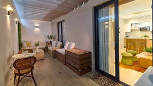A modern interior with a sofa, wooden side table, wicker chairs, and a kitchen visible through glass doors. - Peaceful Retreat Downtownsd Hottub Gym Family (Santo Domingo)