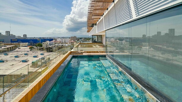 A rooftop pool with a glass barrier, wooden deck, and a city view. - Peaceful Retreat Downtownsd Hottub Gym Family (Santo Domingo)